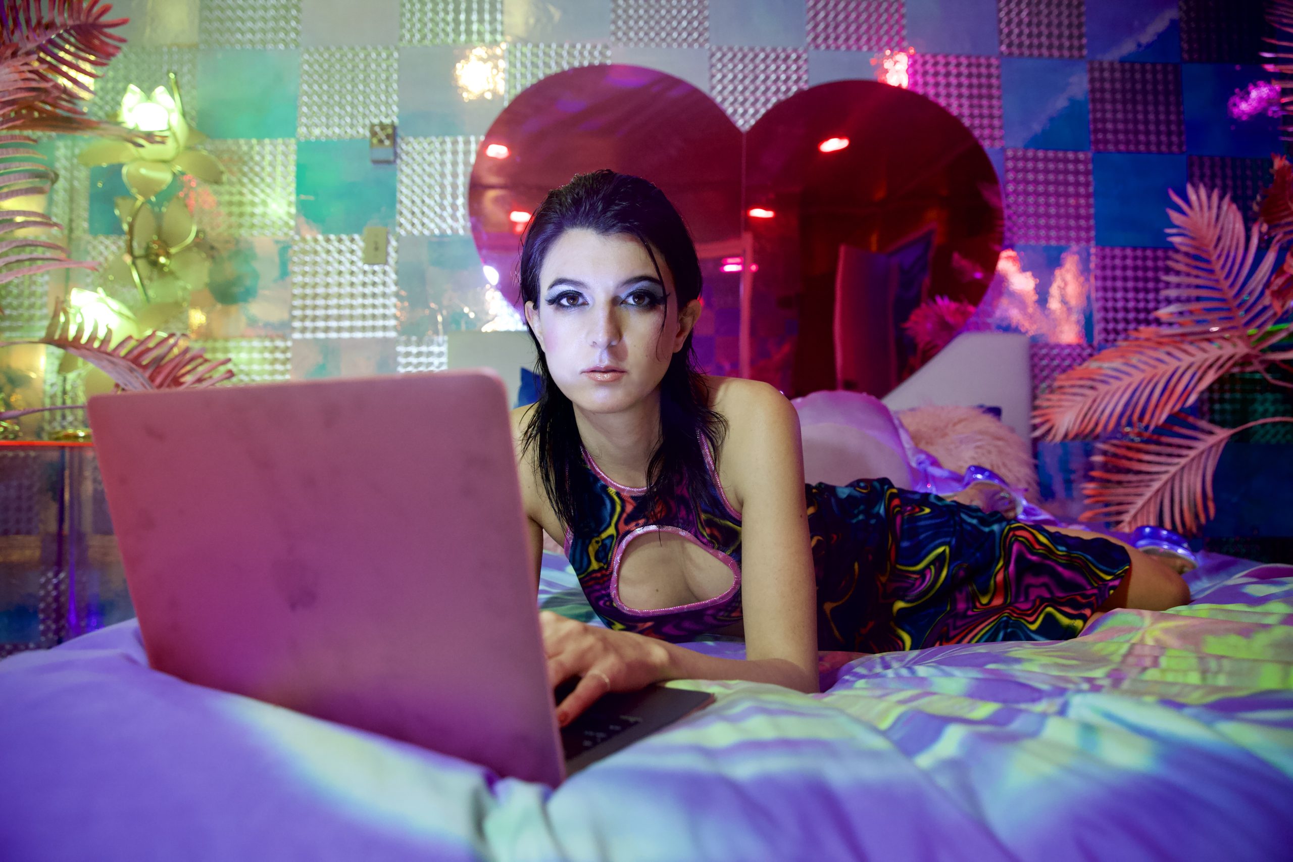 Isa Mazzei lays in bed and types on a hot pink laptop.